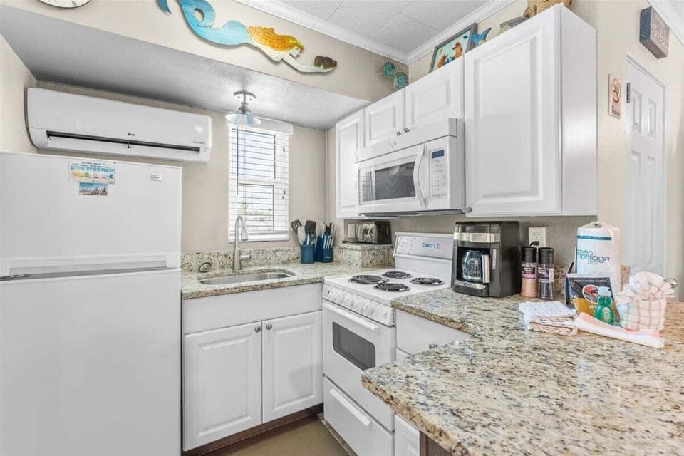 Fully equipped kitchen with white cabinets, granite counters, stove, microwave, fridge, and coffee maker — everything you need for a home-cooked beach meal.