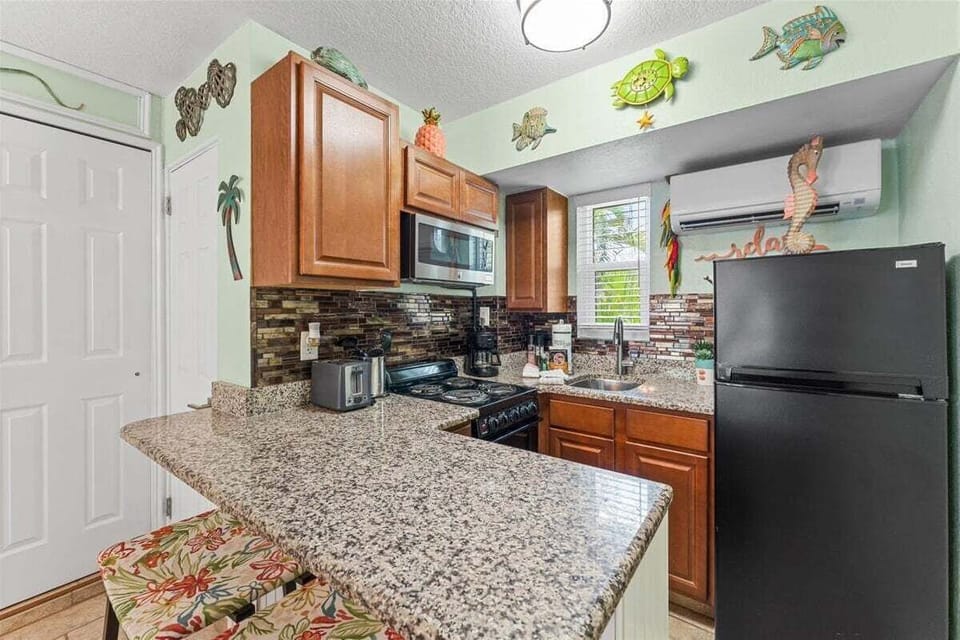 Fully equipped kitchen with granite counters, mosaic tile backsplash, stove, microwave, and fridge — plus a breakfast bar for casual dining with a side of tropical charm.