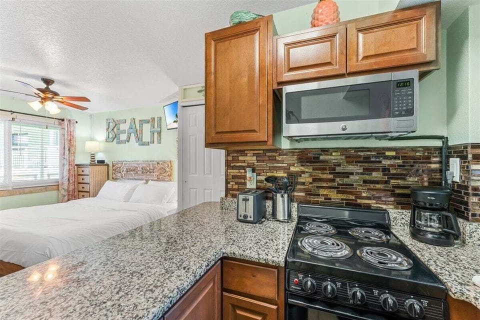 Fully equipped kitchen with granite counters, mosaic tile backsplash, stove, microwave, and fridge — plus a breakfast bar for casual dining with a side of tropical charm.