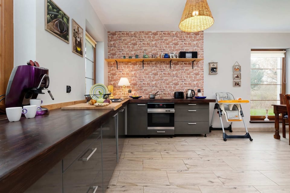 A modern kitchen with black cabinets, a wooden countertop, and a rustic brick backsplash, adjacent to the dining area.