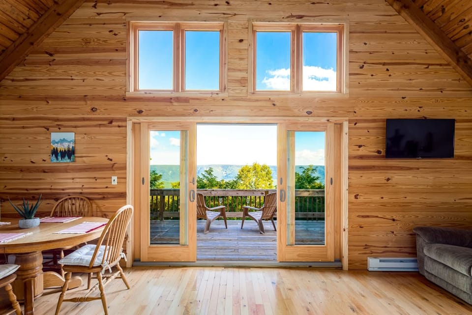 rustic cabin interior with large windows opening to a deck overlooking forested hills