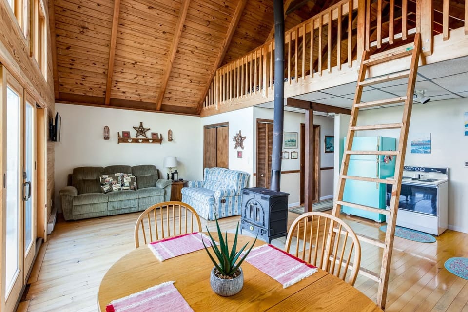 Cozy cabin interior with vaulted wood ceilings and a loft accessed by a wooden ladder.