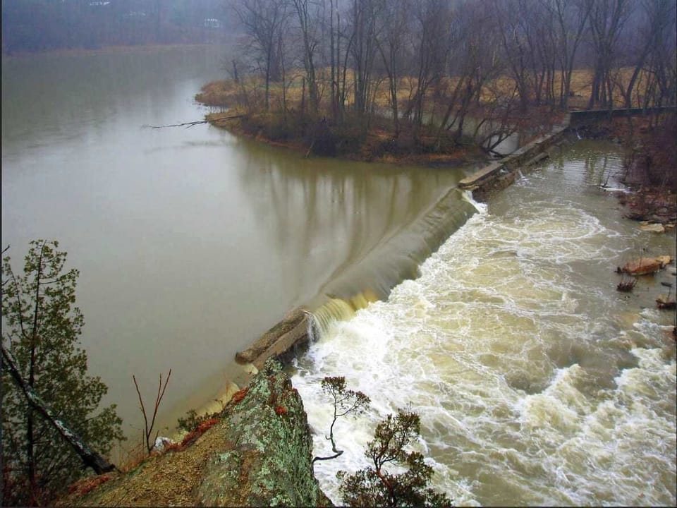 View of a river dam with surrounding bare trees and flowing water creating a natural landscape.