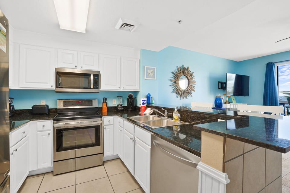 Your fully equipped kitchen awaits with granite counters, stainless appliances, and coastal blue walls creating the perfect space for preparing memorable meals.