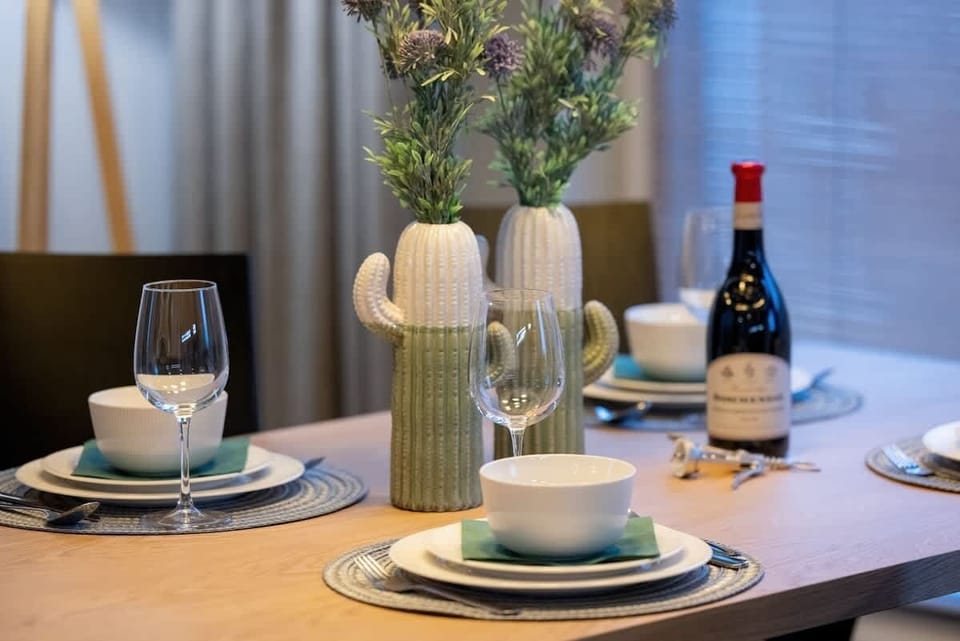 A close-up of a beautifully set dining table with wine glasses, plates, a bottle of wine, and a flower vase as decoration.
