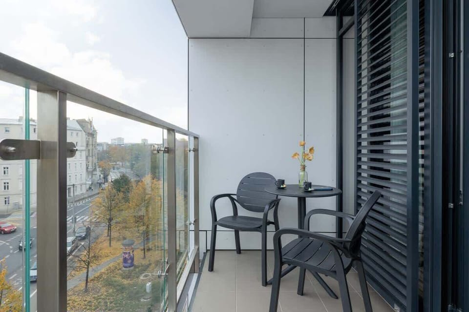 A narrow balcony with small table with two chairs, and views of greenery and the surrounding area.