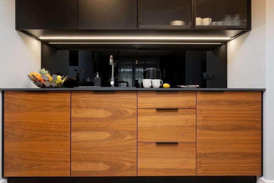 Modern fully equipped kitchen with appliances such as dishwasher, oven, fridge and induction hob. The lower cabinets are wood coloured and the upper cabinets are black to match the black worktop.