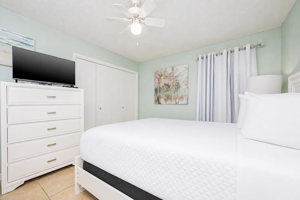 Inviting guest bedroom featuring a plush queen bed, a large TV, and soothing green walls for a relaxing stay