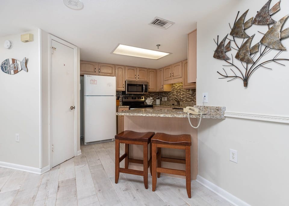 The kitchen features light wood cabinetry, a granite countertop, and a breakfast bar with two wooden stools for casual dining