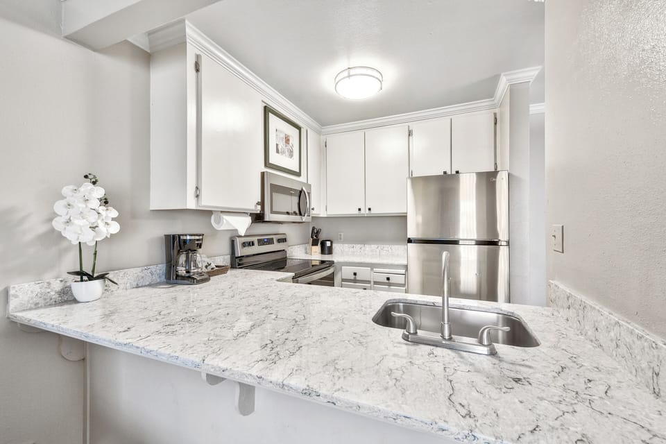 Cook comfortably on bright counters with stainless appliances and sink.