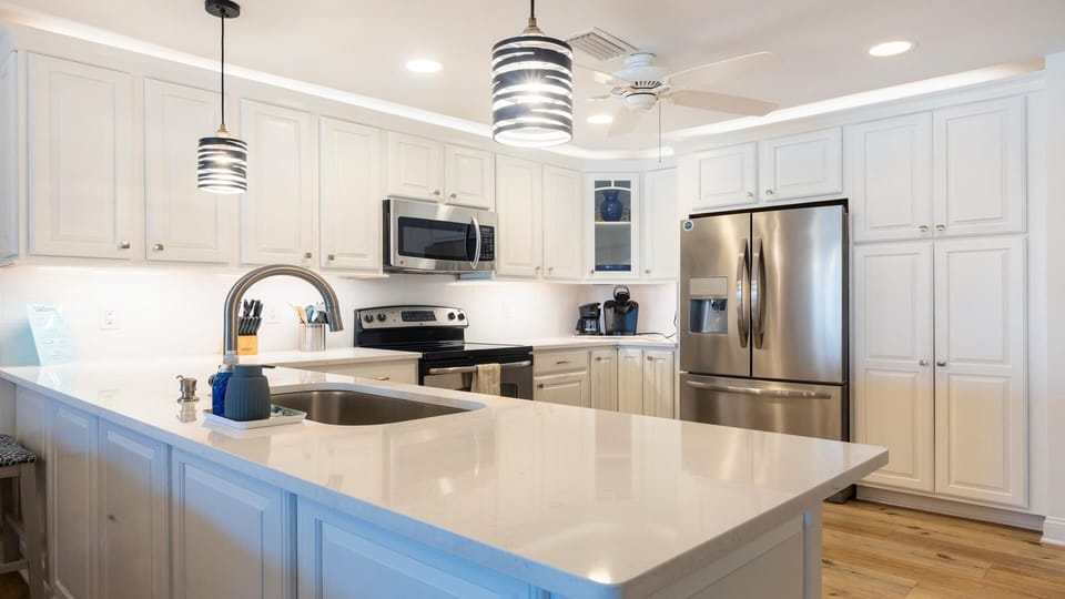 White cabinetry and quartz countertops surround stainless steel appliances in the bright kitchen.