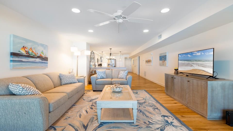 Light wood flooring extends through the living area with beige sofas, patterned rug, and a TV on a textured cabinet.