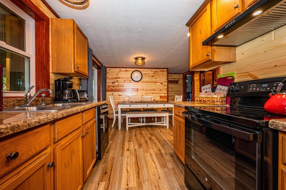 Galley kitchen with honey oak cabinets, granite-patterned counters, black appliances, and wood plank flooring.