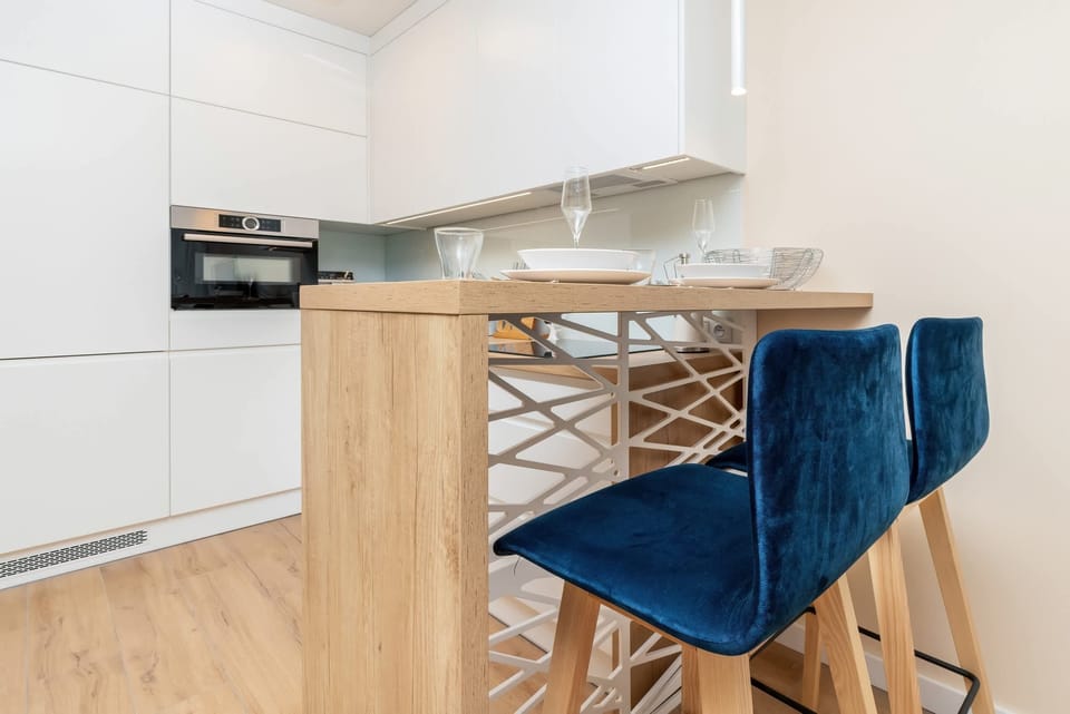 A sleek, white kitchen with minimalist cabinetry and a cozy dining area featuring light wood accents and subtle decorative touches.