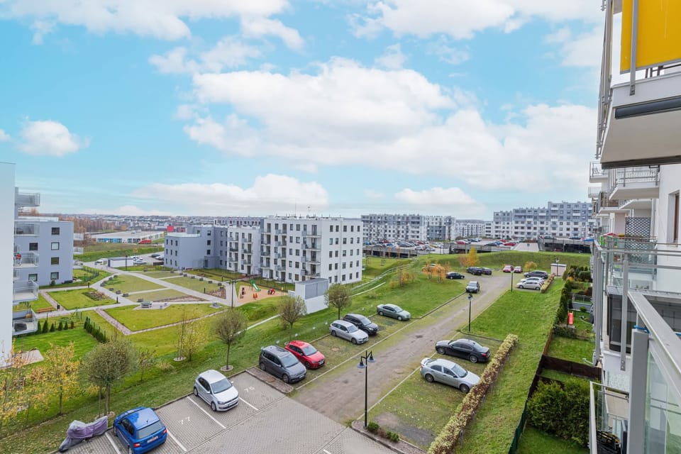A scenic view of a residential area, captured from a balcony. It showcases modern apartment buildings, green spaces, and parking areas.