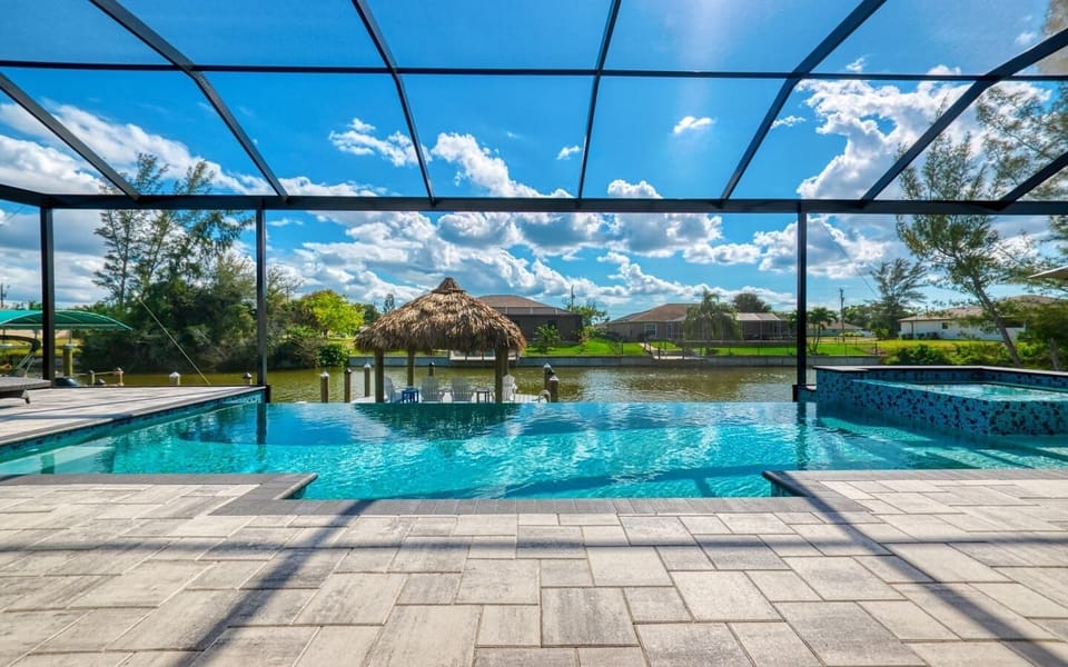 Pool and spa inside the screened cage with the thatched tiki hut and boat dock visible along the canal
