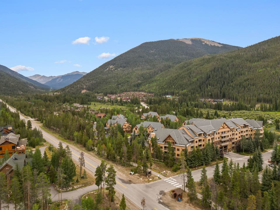 A mountain resort complex nestled in a forested valley, surrounded by towering peaks and evergreens, offering a scenic alpine retreat.