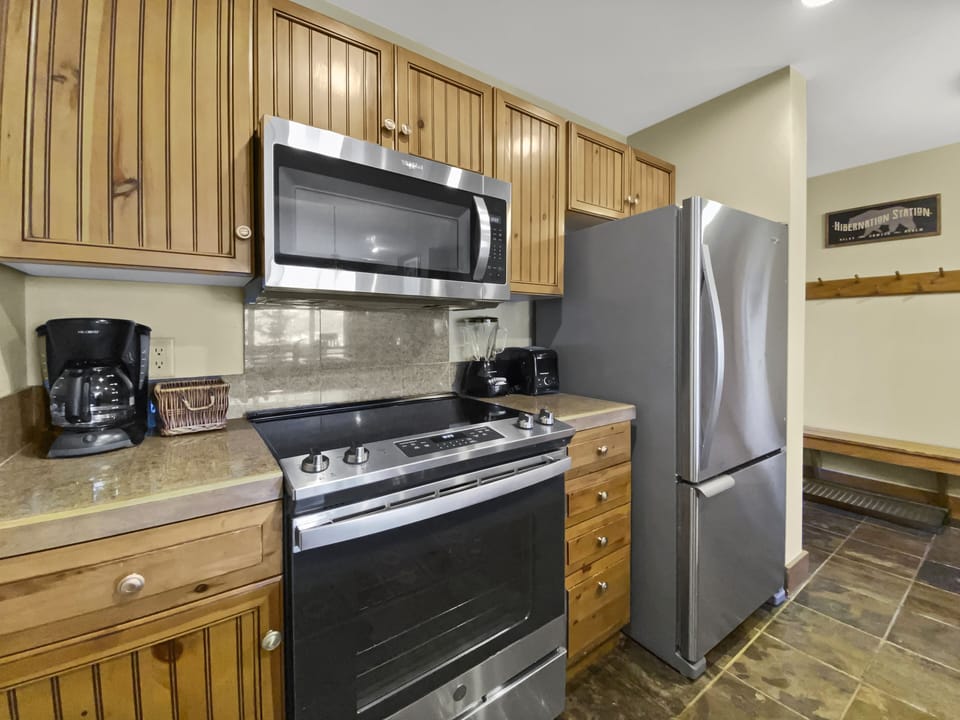 A modern kitchen featuring a stainless steel stove, microwave, and refrigerator. Wooden cabinets and a coffee maker are also visible.