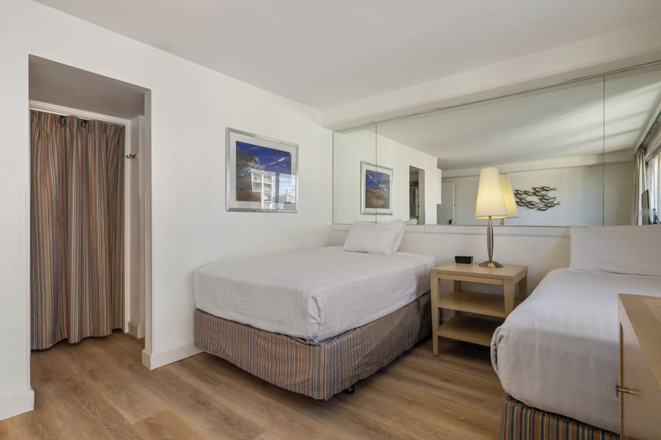 Relax in your spacious bedroom featuring two comfortable beds, warm wood floors, and thoughtful touches like bedside lighting for a restful night's sleep.