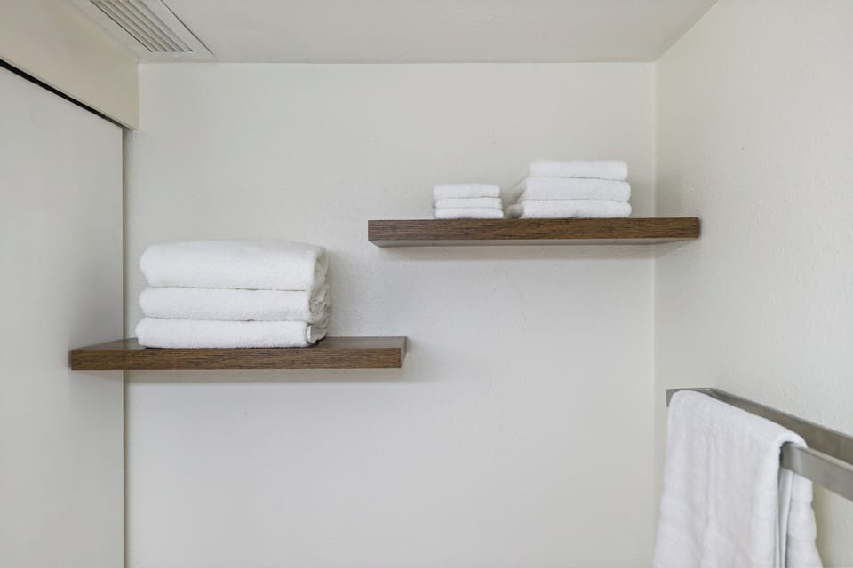 Fresh towels await you on elegant floating shelves, creating a clean, organized space for your comfort.
