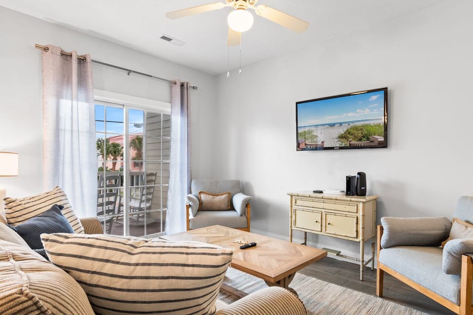 Relax in your bright living room with coastal charm, featuring comfortable seating and beach views on the wall-mounted TV.