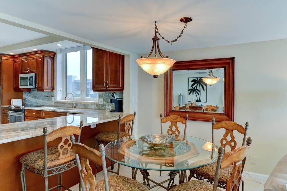 Kitchen counter with marble surface extends into bar seating with wrought iron and patterned cushions.
