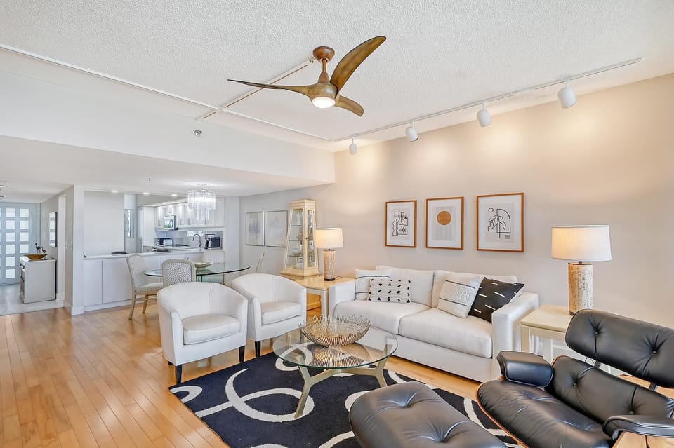 Living room with hardwood floors, white sofa, black leather chair, glass coffee table, and abstract wall art.