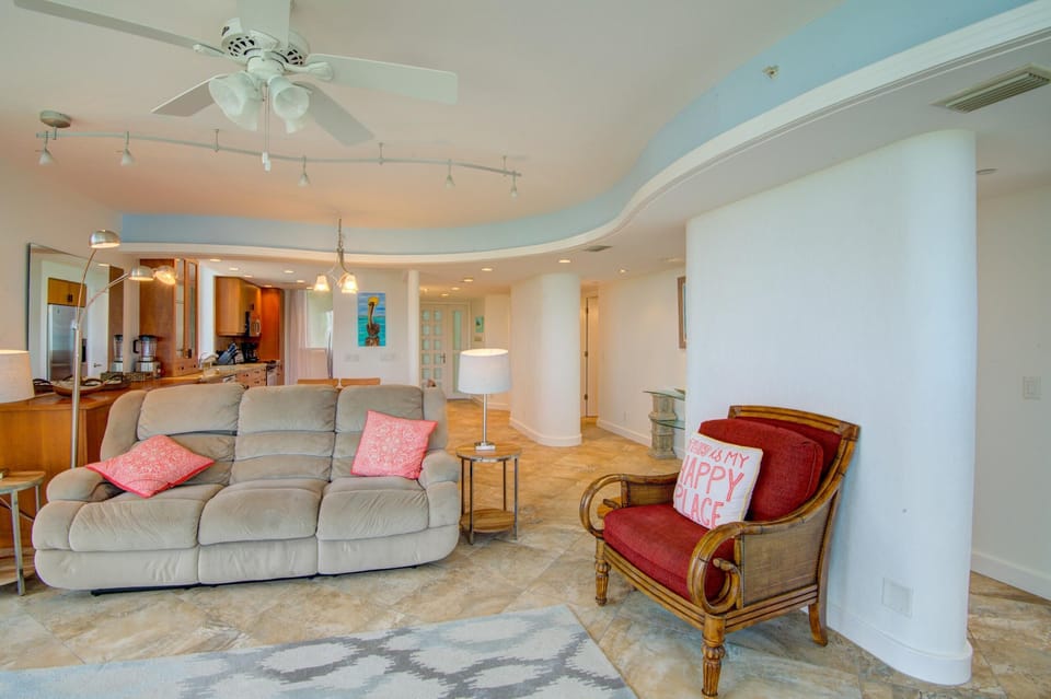 Tiled floors extend through the living room, featuring a beige recliner sofa, wooden armchair, and curved white wall.
