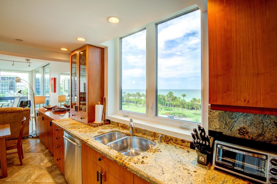 Granite countertop kitchen sink under twin windows framing palm trees and Gulf water views.