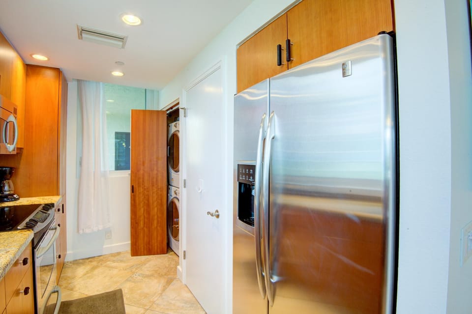 Galley kitchen with granite counters, stainless steel appliances, warm wood cabinets, and stacked washer-dryer closet.