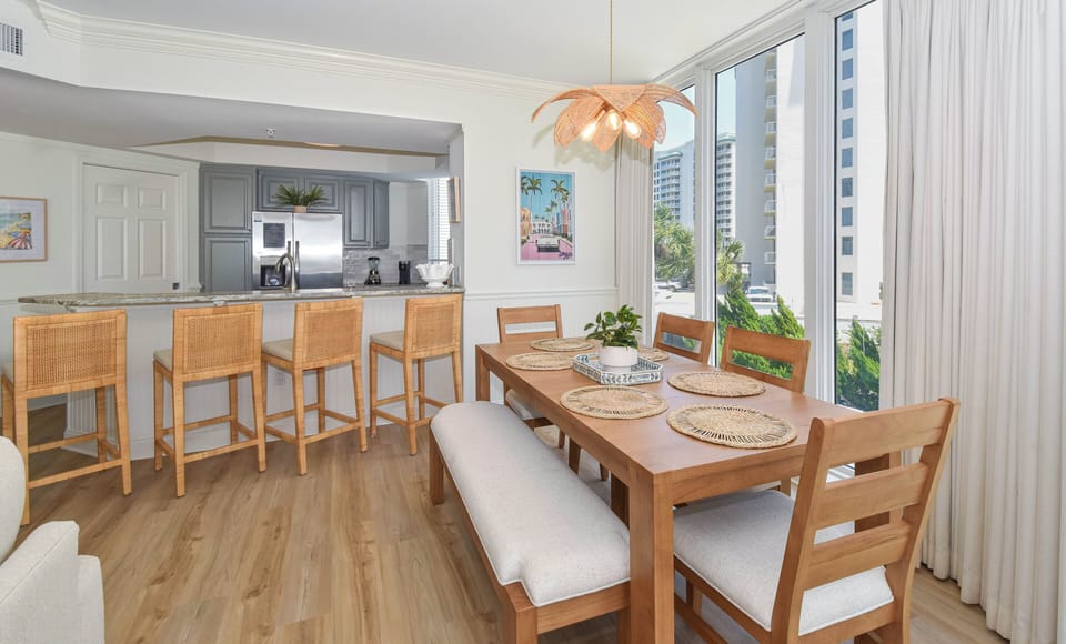 Your bright, open dining area flows seamlessly into a fully equipped kitchen, with floor-to-ceiling windows framing tropical palm views and plenty of space to gather for meals together.