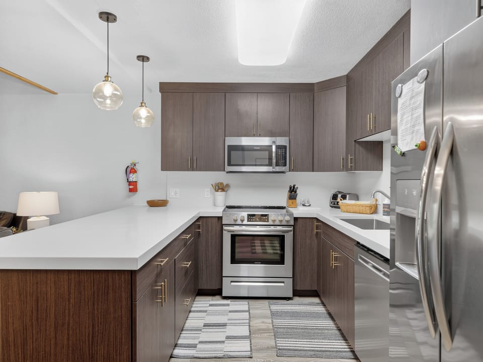 Step into your sleek, fully equipped kitchen featuring dark wood cabinetry, gleaming stainless steel appliances, and bright quartz countertops. Everything you need to cook and relax in style awaits you here.