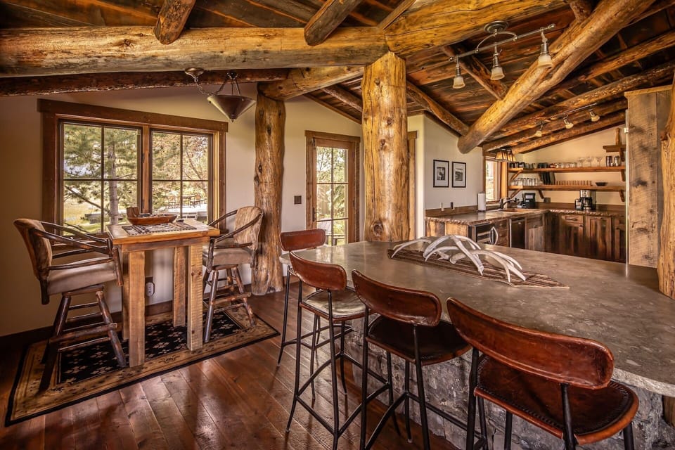 Gather around the handcrafted stone island under stunning log beam ceilings. Your mountain retreat features rustic charm with modern comforts, where natural wood and leather seating invite conversation and connection.