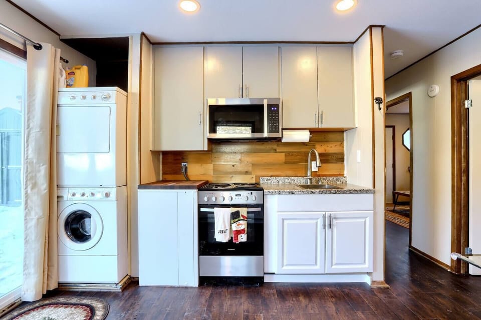 - Make meals with ease in a fully equipped kitchen featuring granite countertops & gas stove
- Enjoy added convenience with in unit laundry tucked neatly beside the cooking area
- Wood backsplash and soft lighting create a warm, modern cabin vibe