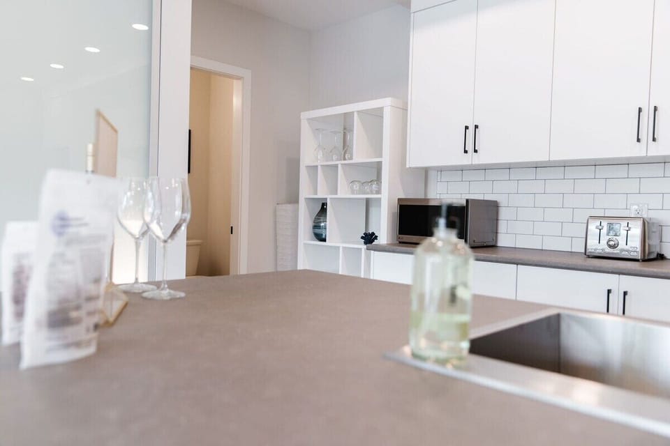 Prepare meals in style with the sleek gray countertops and white cabinets. The soap dispenser keeps things tidy, while wine glasses are ready for your next toast. A clean, spacious kitchen for cooking and relaxing.
