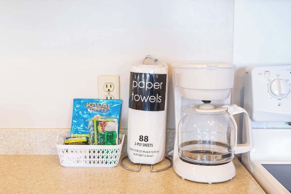 A coffee maker with complimentary coffee supplies and paper towels on the kitchen counter.