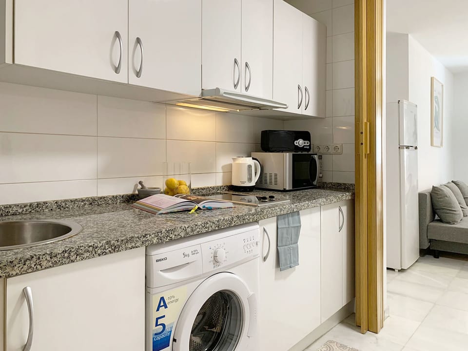 Modern and compact kitchen with glossy white cabinets, granite countertop, integrated appliances, and a washing machine for a functional small-space design.