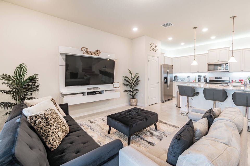 Experience a stylish living area with plush sofas, decorative cushions, and a striking coffee table for relaxation. The open layout flows into a well-equipped kitchen, beautifully lit by modern pendant lights.