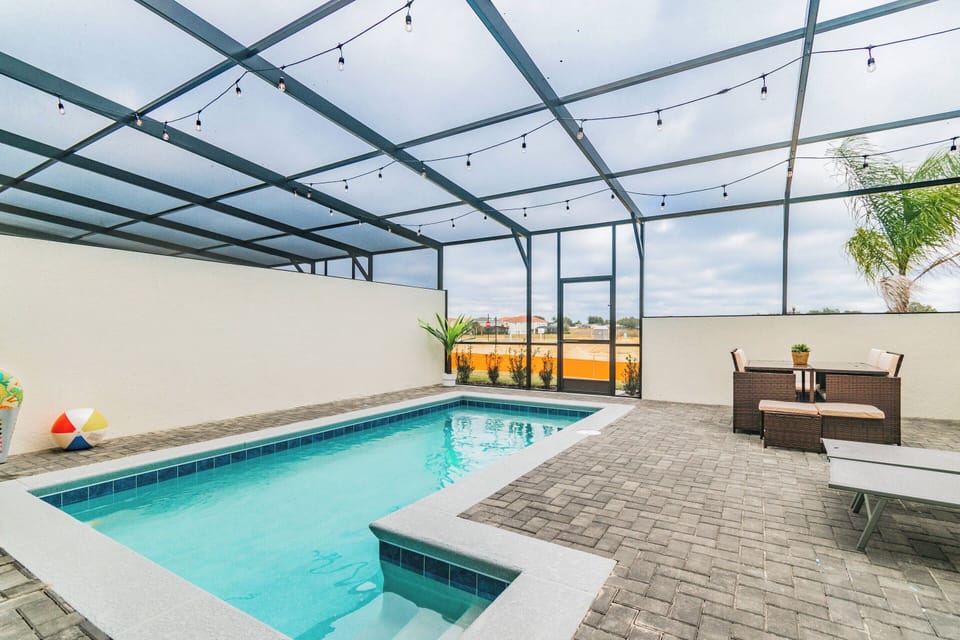 Step into a private paradise featuring a sparkling pool framed by sleek pavers and a charming lounge area. The modern outdoor space is enhanced by twinkling string lights, perfect for evening relaxation or sunny afternoons.