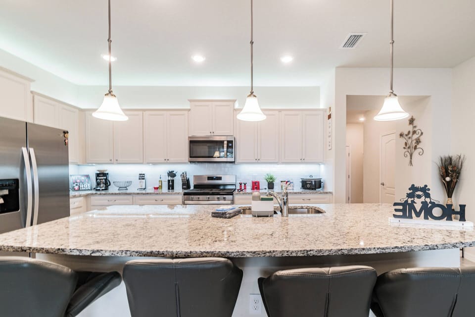 This stylish kitchen boasts a spacious granite island, ideal for culinary creativity, enhanced by warm under-cabinet lighting. Modern stainless-steel appliances and chic bar stools set the perfect scene for gatherings.