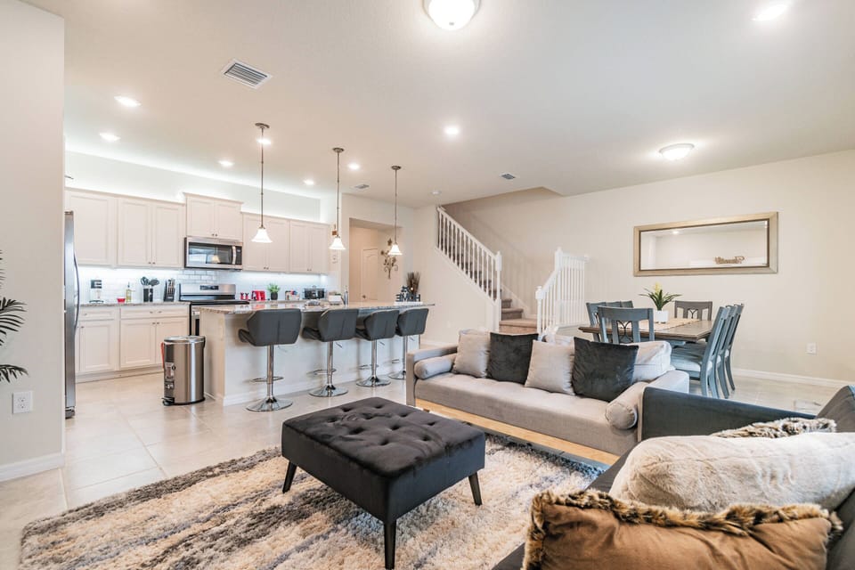 Enjoy the spacious living area with a plush sectional sofa and stylish ottoman, ideal for relaxation. The sleek kitchen, complete with modern bar stools and bright lighting, invites you to unwind or effortlessly prepare meals.