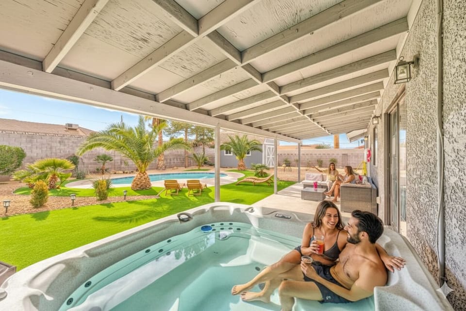  Relax in your private outdoor oasis! This inviting patio features a bubbling hot tub under a shaded pergola, perfect for unwinding. Enjoy comfortable outdoor seating and stunning views of the lush backyard and pool beyond.