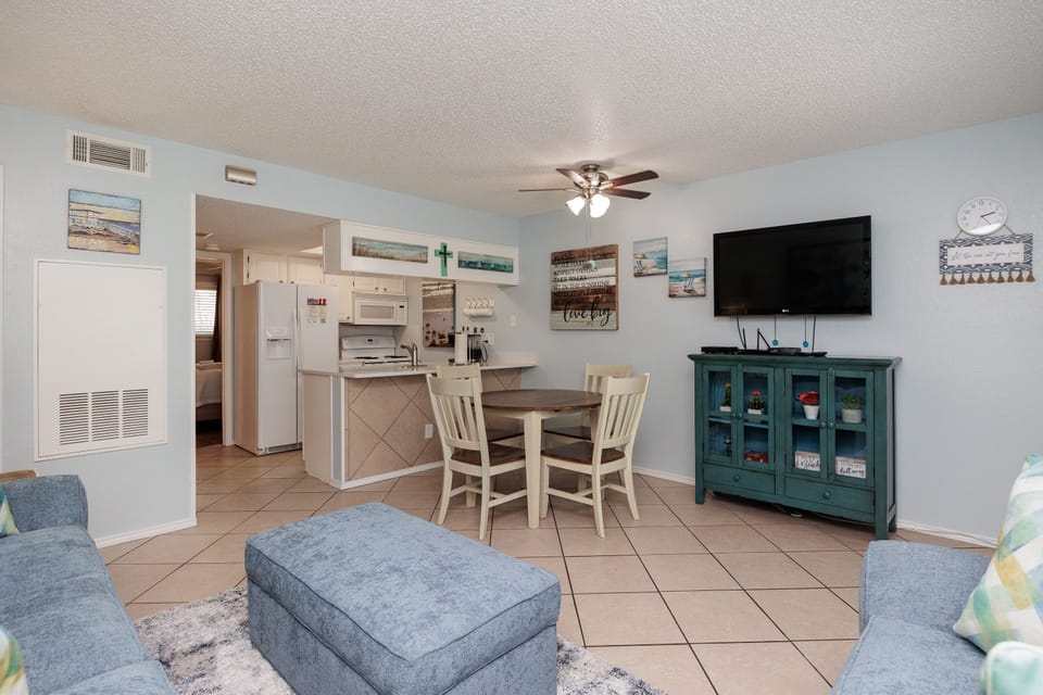 Relax in your bright, coastal-themed living space featuring comfortable seating, beach artwork, and an open kitchen perfect for vacation meals.
