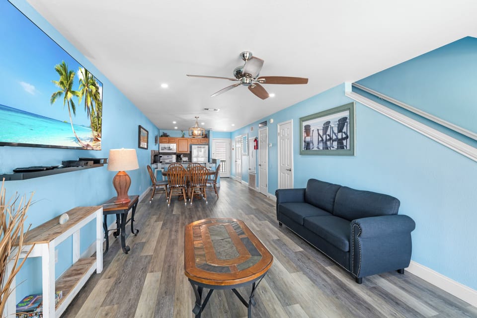 Relax in your bright, coastal-themed living space with ceiling fans, comfortable seating, and an open layout connecting to your kitchen.