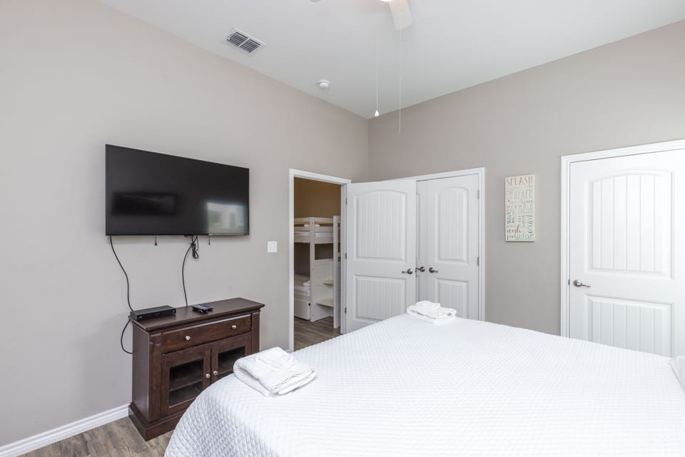 Unwind in your serene bedroom with cozy bedding, entertainment center, and glimpse of bunk beds through the doorway.