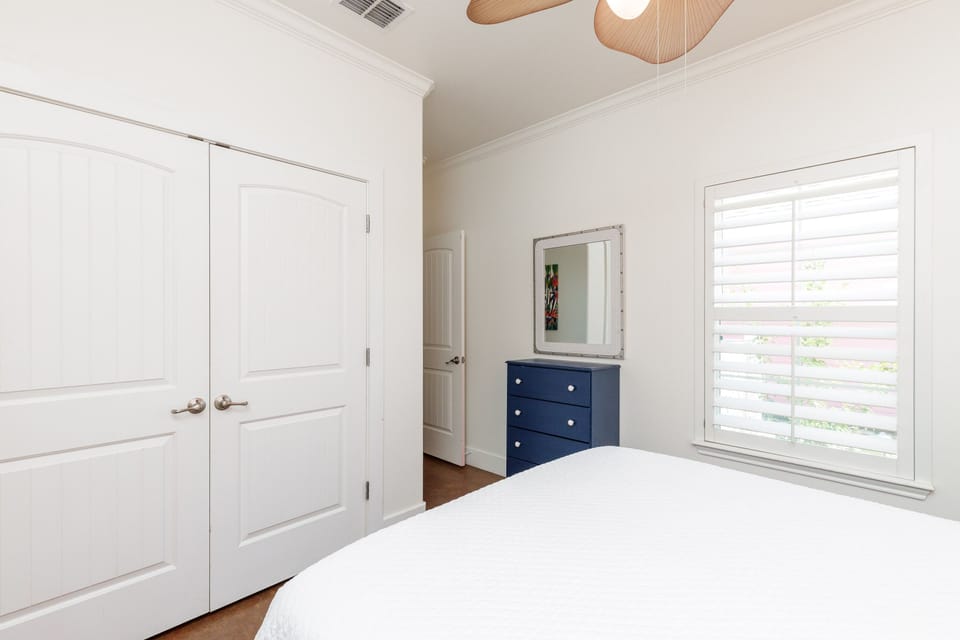 Your bright bedroom features crisp white linens, stylish navy accents, and natural light streaming through plantation shutters for peaceful mornings.