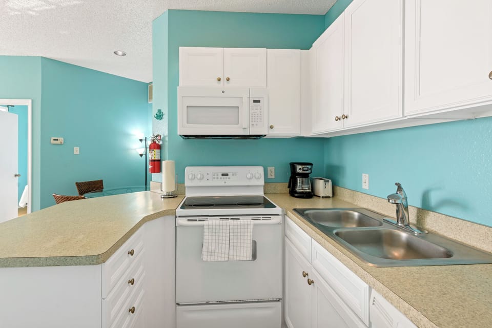 Your bright, fully-equipped kitchen awaits with white cabinets, modern appliances, and cheerful turquoise walls to inspire your culinary adventures.