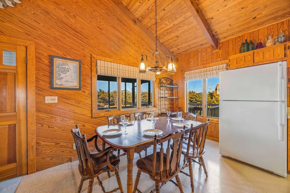 Step into your cozy cabin dining room where warm wood surrounds you and natural light streams through multiple windows as you gather for memorable meals.
