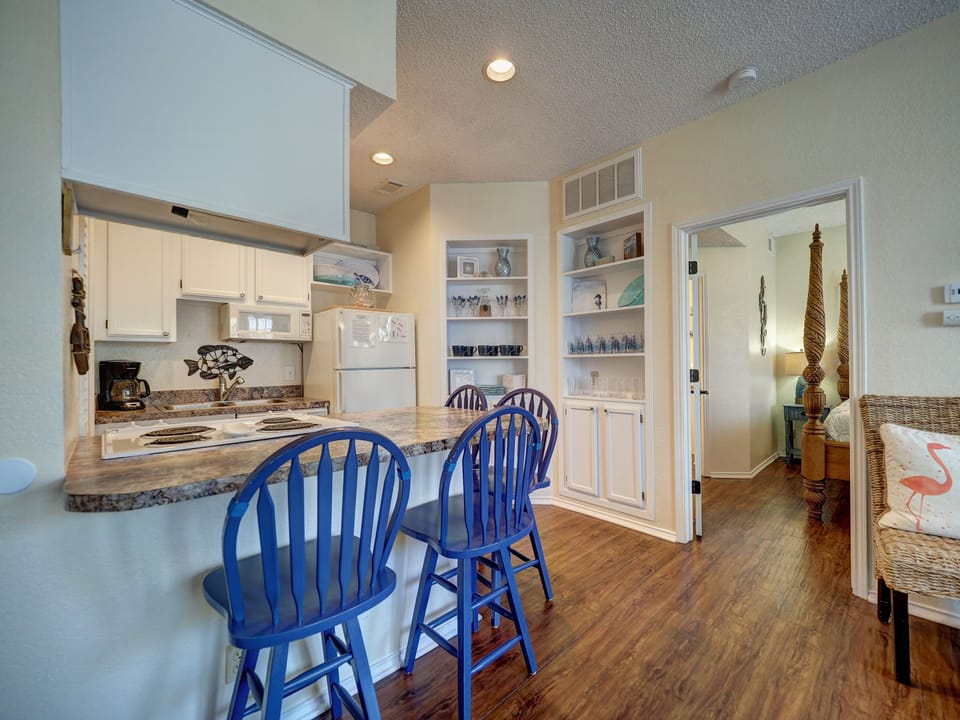 Your bright kitchen flows seamlessly into the living area, complete with a breakfast bar and charming blue Windsor chairs for casual dining.