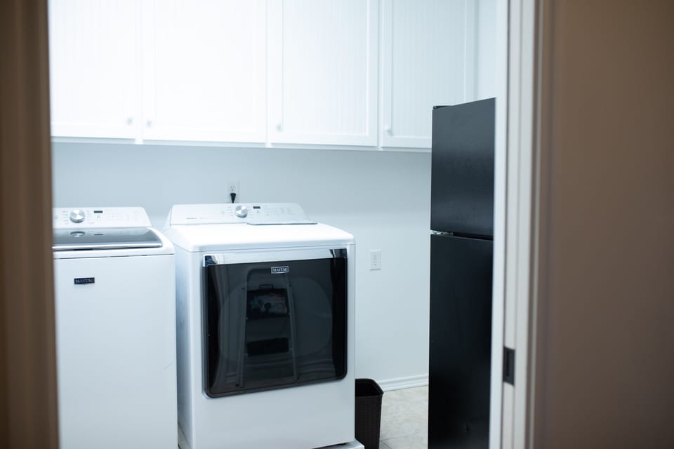 Laundry room with washer / drier, storage space, and extra fridge.